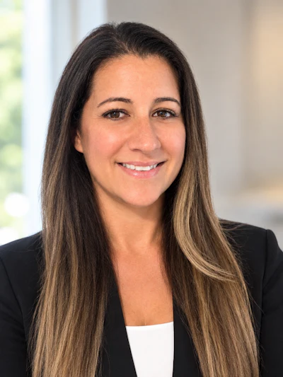 Professional headshot of a woman with long dark hair wearing a black blazer and white top, smiling at the camera