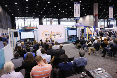 Crowded convention center floor with attendees seated facing Innovation Edge stage presentation and blue booth displays.