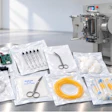 Sterile medical supplies and surgical instruments including tubing, scissors, circuit board, and packaging displayed with laboratory equipment in background